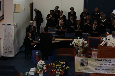 Church choir singing on stage with a conductor and floral arrangements in front