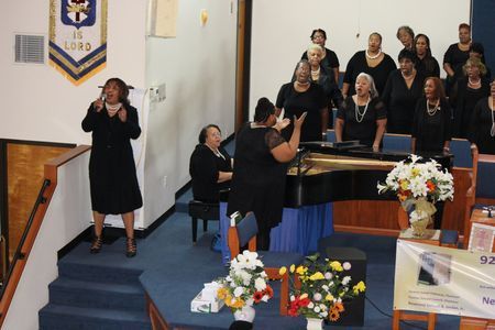 Choir performing in a church sanctuary with flowers and a sign language interpreter nearby