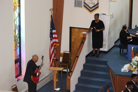 People speaking on a church stage beside a staircase and American flag