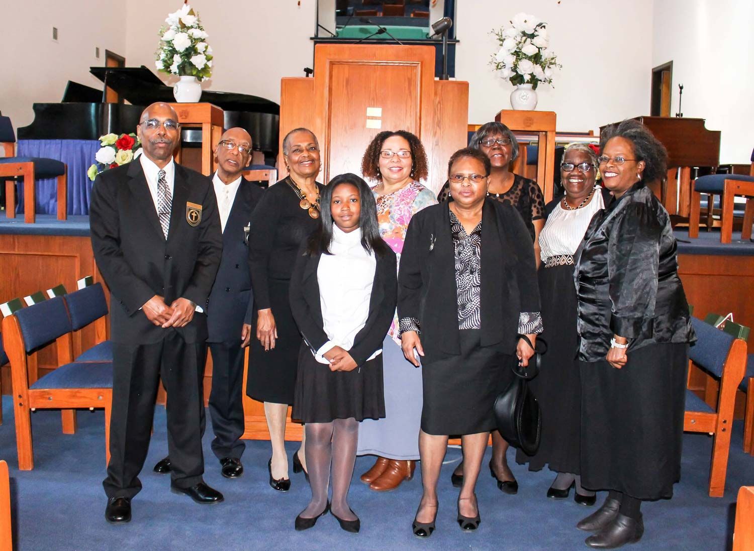 Group of people posing in a church sanctuary, dressed in black and white attire.