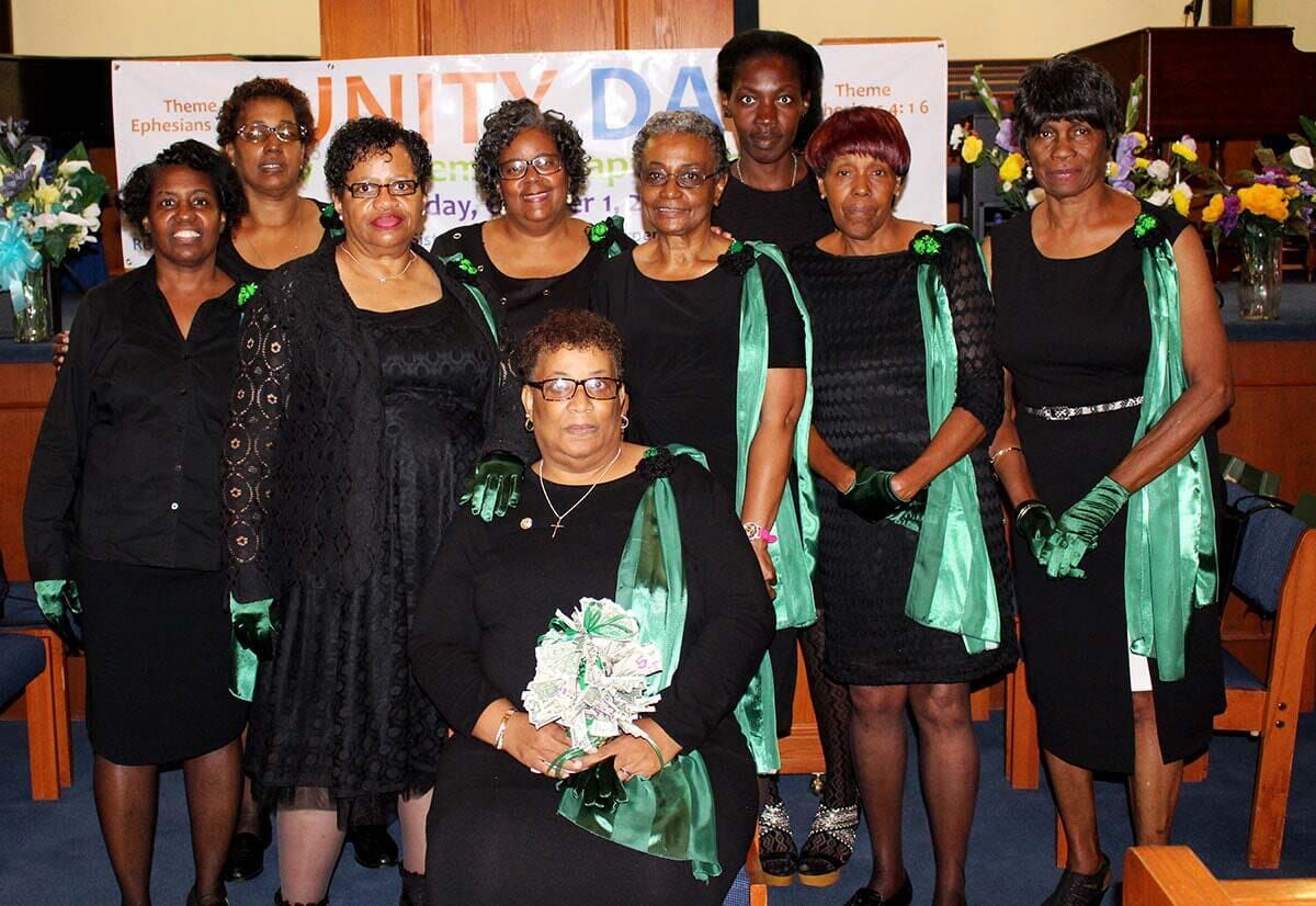 Group portrait of people in black and green outfits posing indoors on a stage