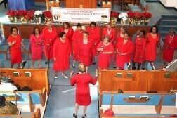 Choir in red robes standing in a church, facing a conductor at the front.