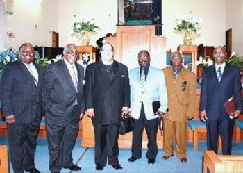 Six men in suits standing together in a church sanctuary.