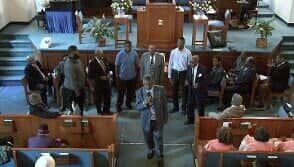 People standing in a church-like hall near the front stage during a meeting or ceremony.