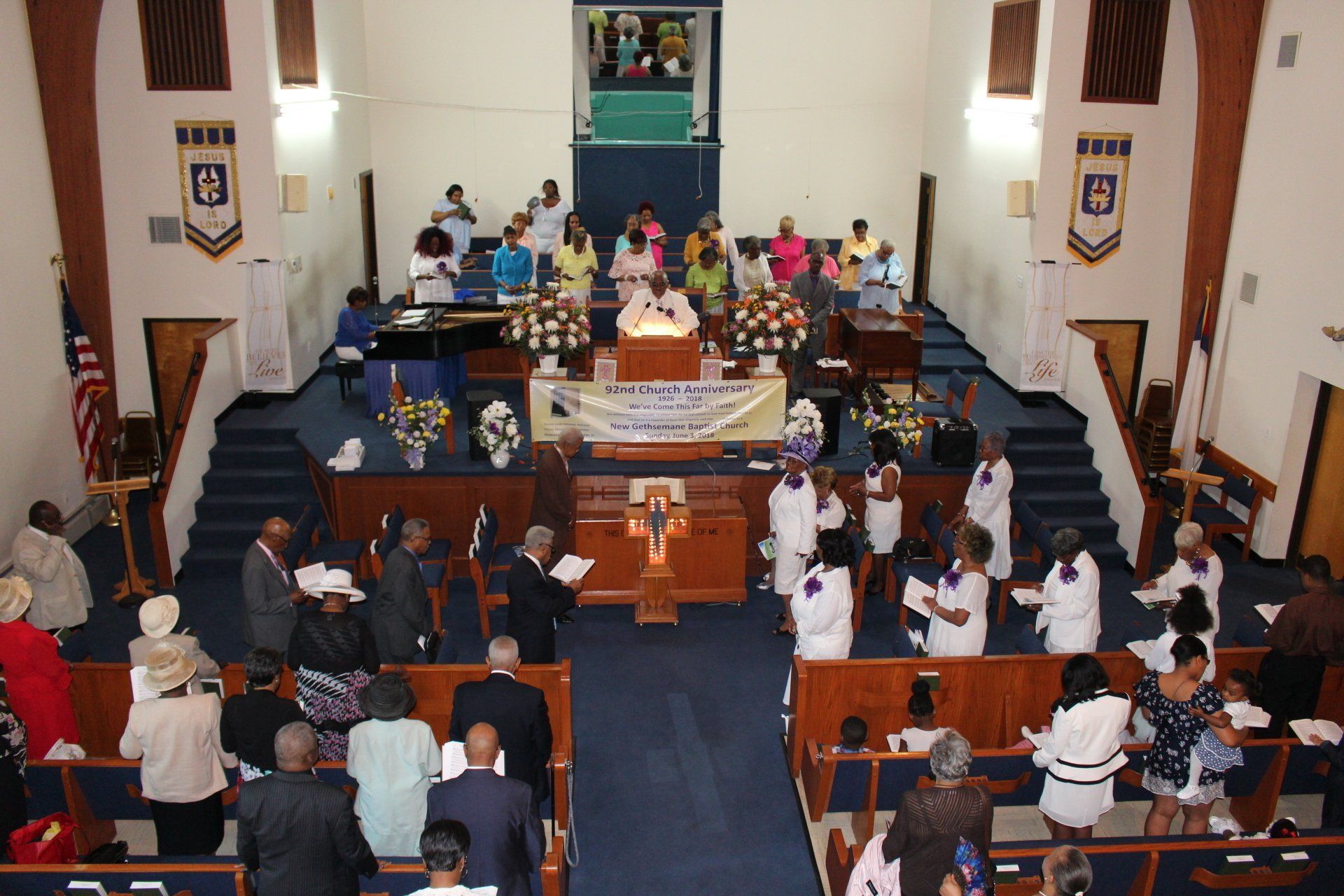 Church service with people seated in pews facing a choir and altar on a raised platform