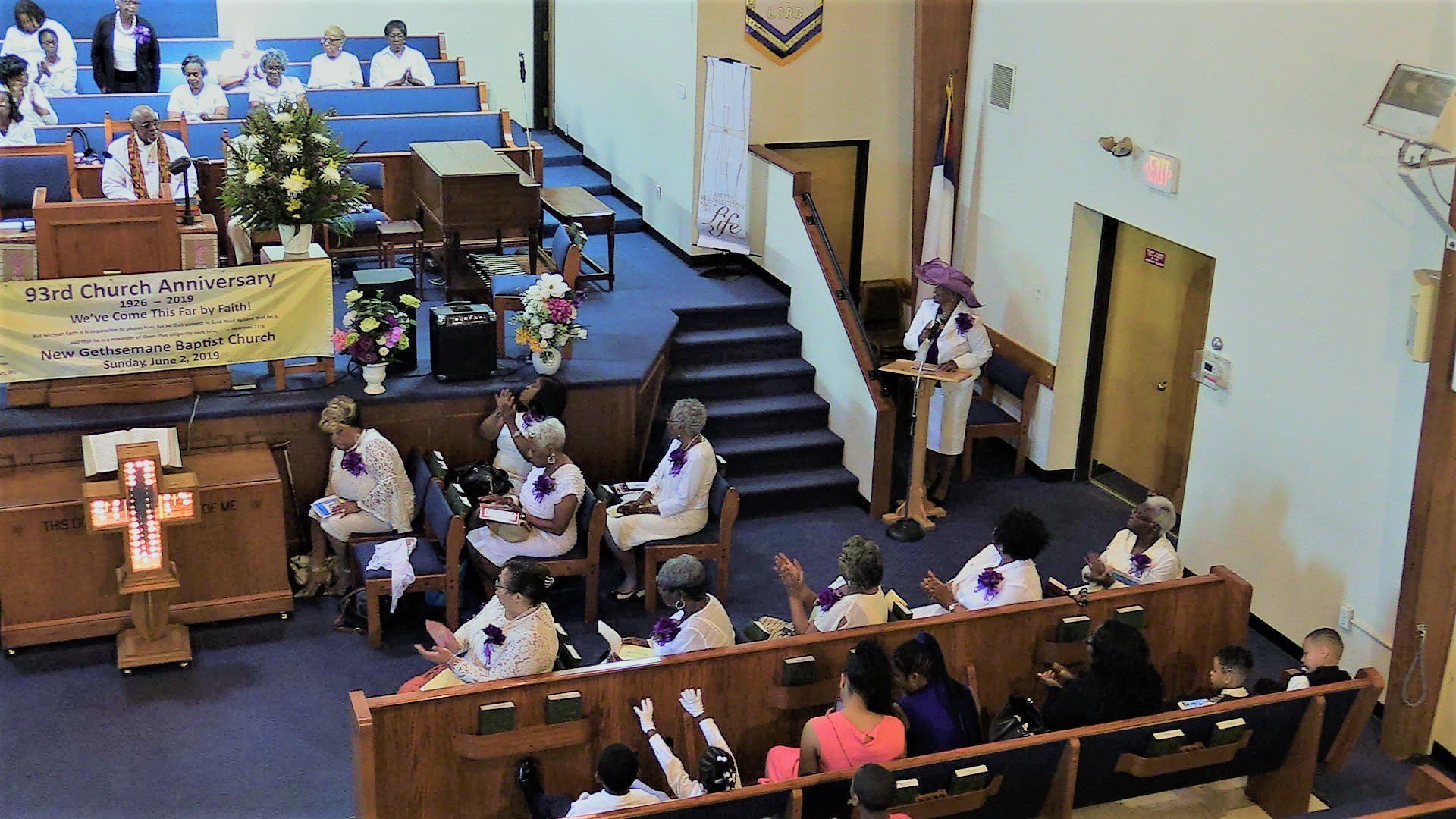 Church sanctuary with seated congregation, choir in blue robes, and people standing near the front steps