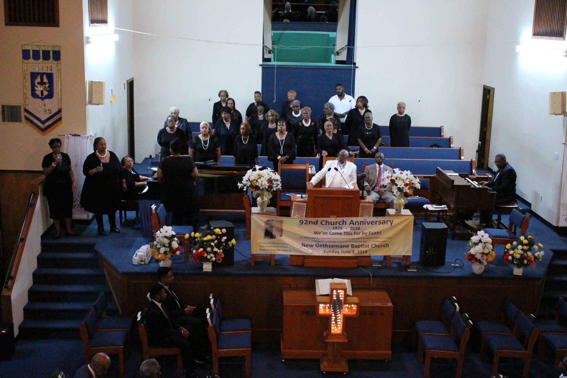 Church sanctuary with people seated and standing on stage around a central banner and floral arrangements
