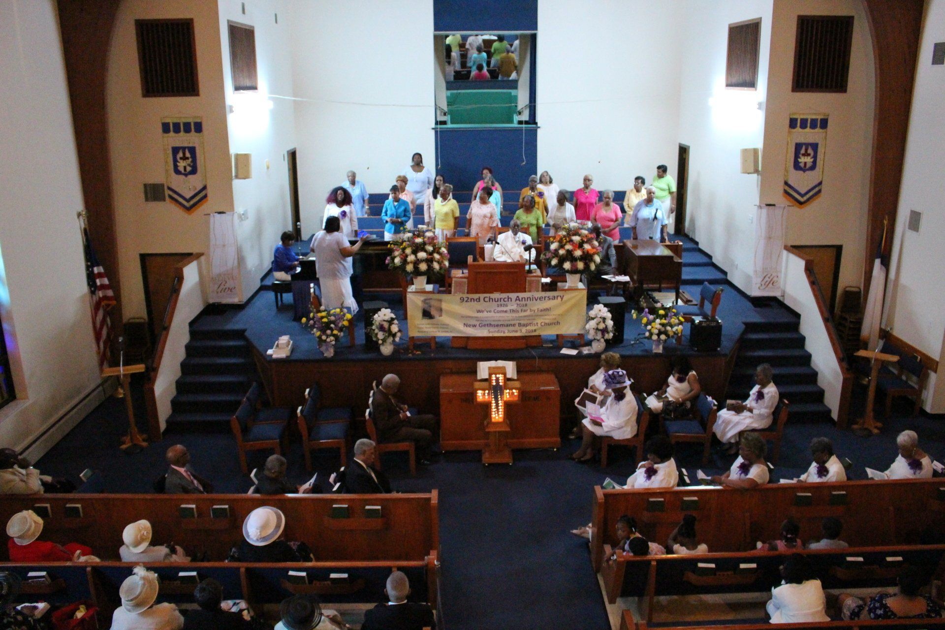 Church service with people seated in pews facing a decorated altar and choir platform.