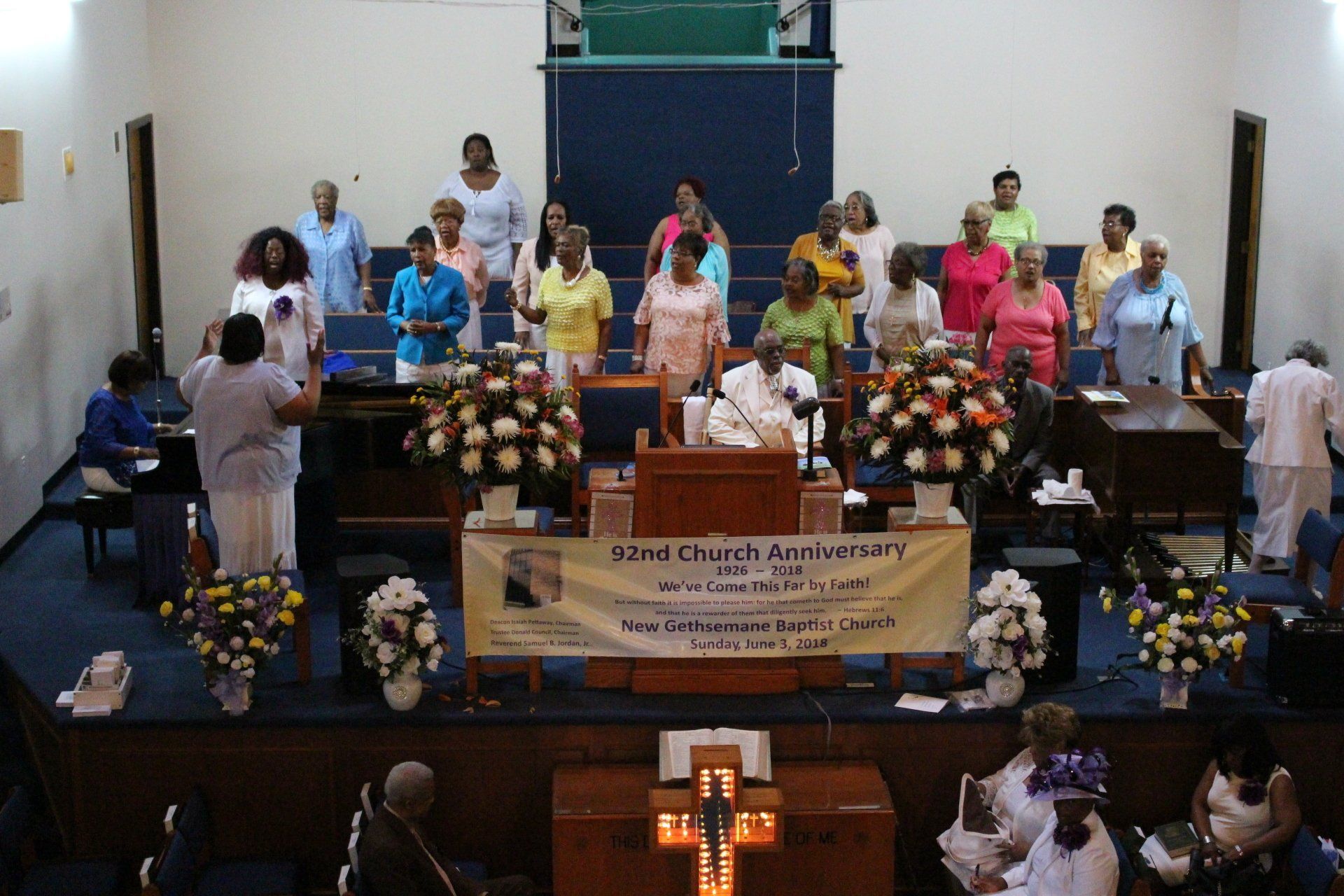 People on a church stage with flowers and a banner during a ceremony or service
