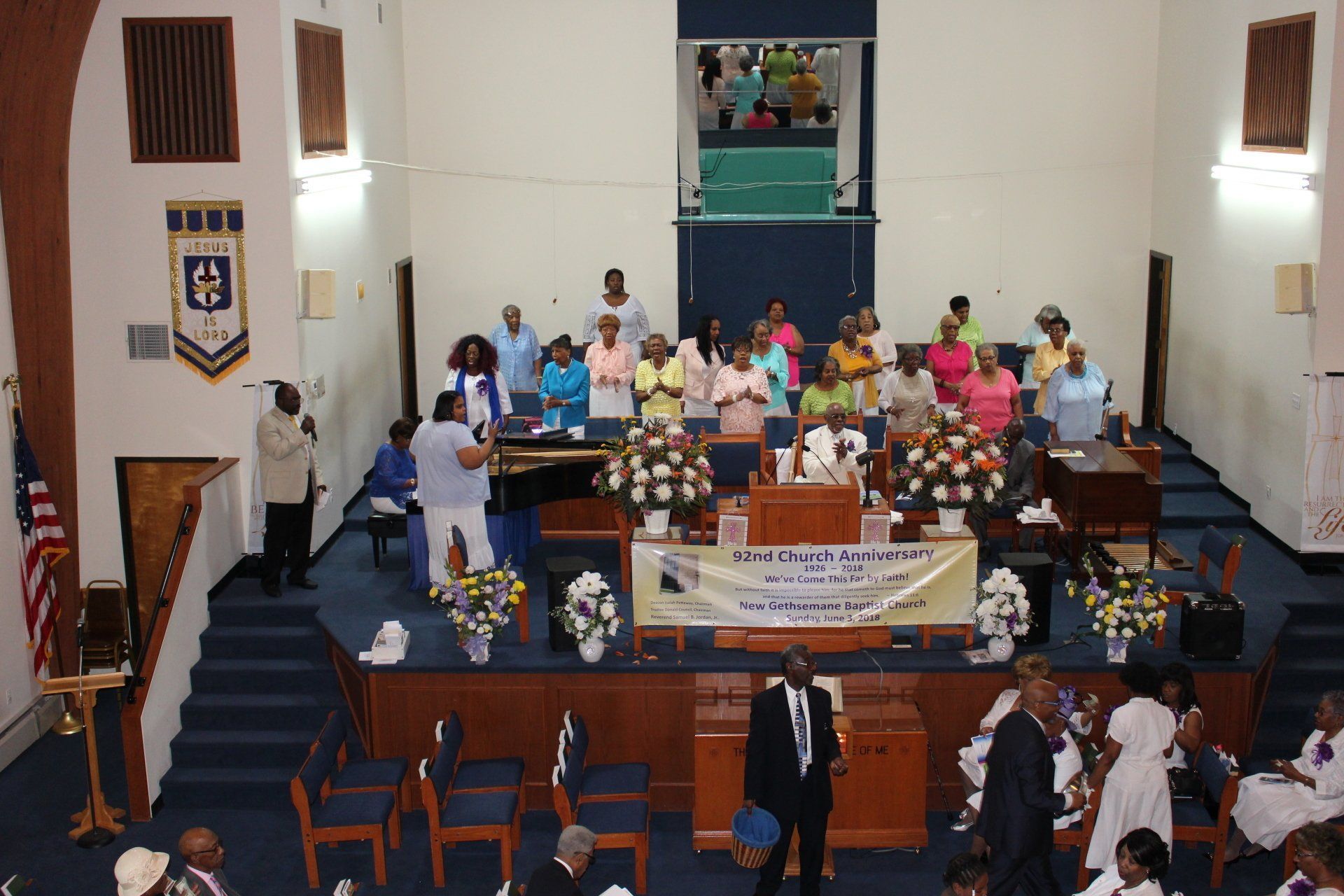 Church interior with a group gathered on the stage behind a pulpit, facing rows of chairs