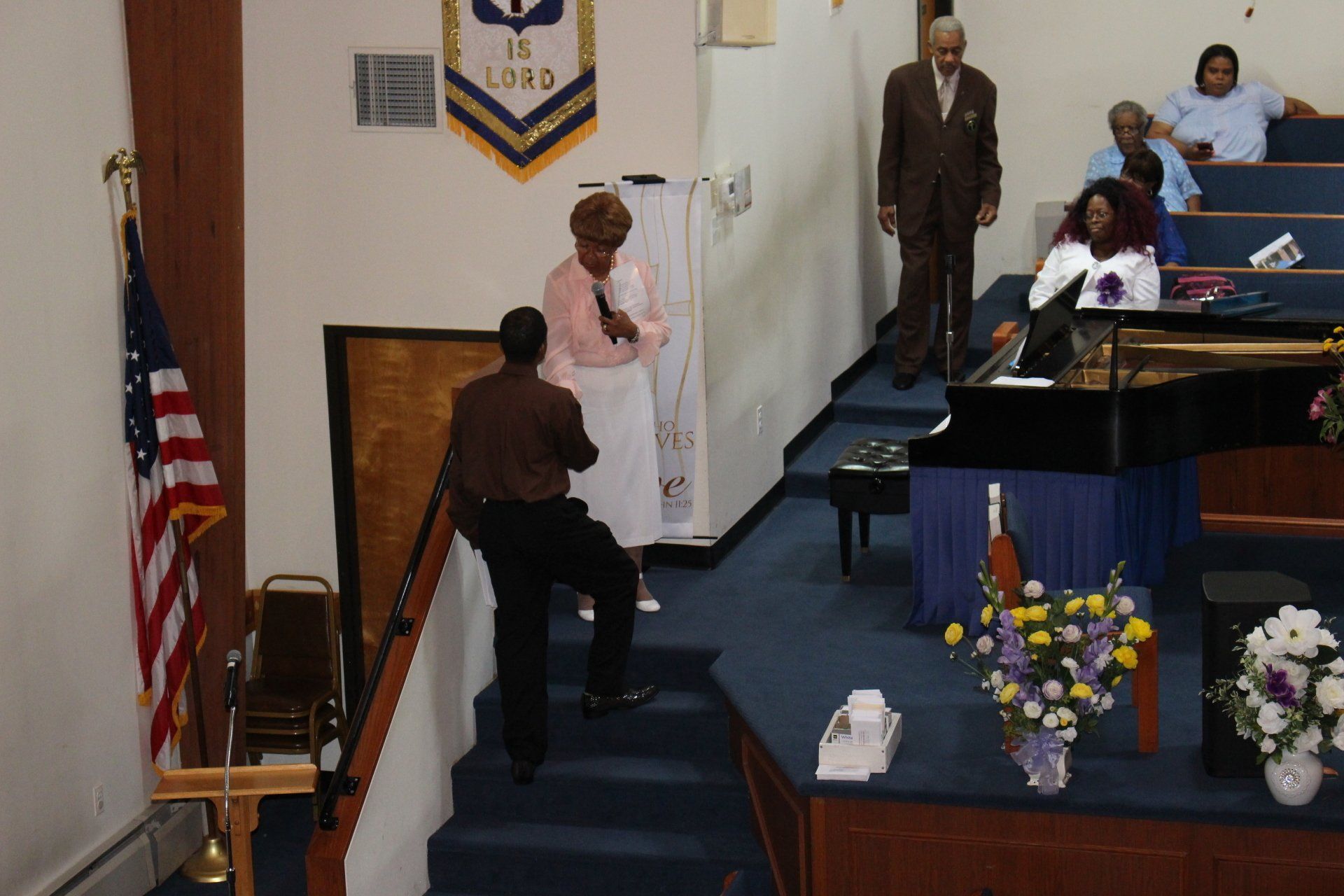 People gathered in a church sanctuary during a ceremony, with a woman onstage and flowers at the podium.
