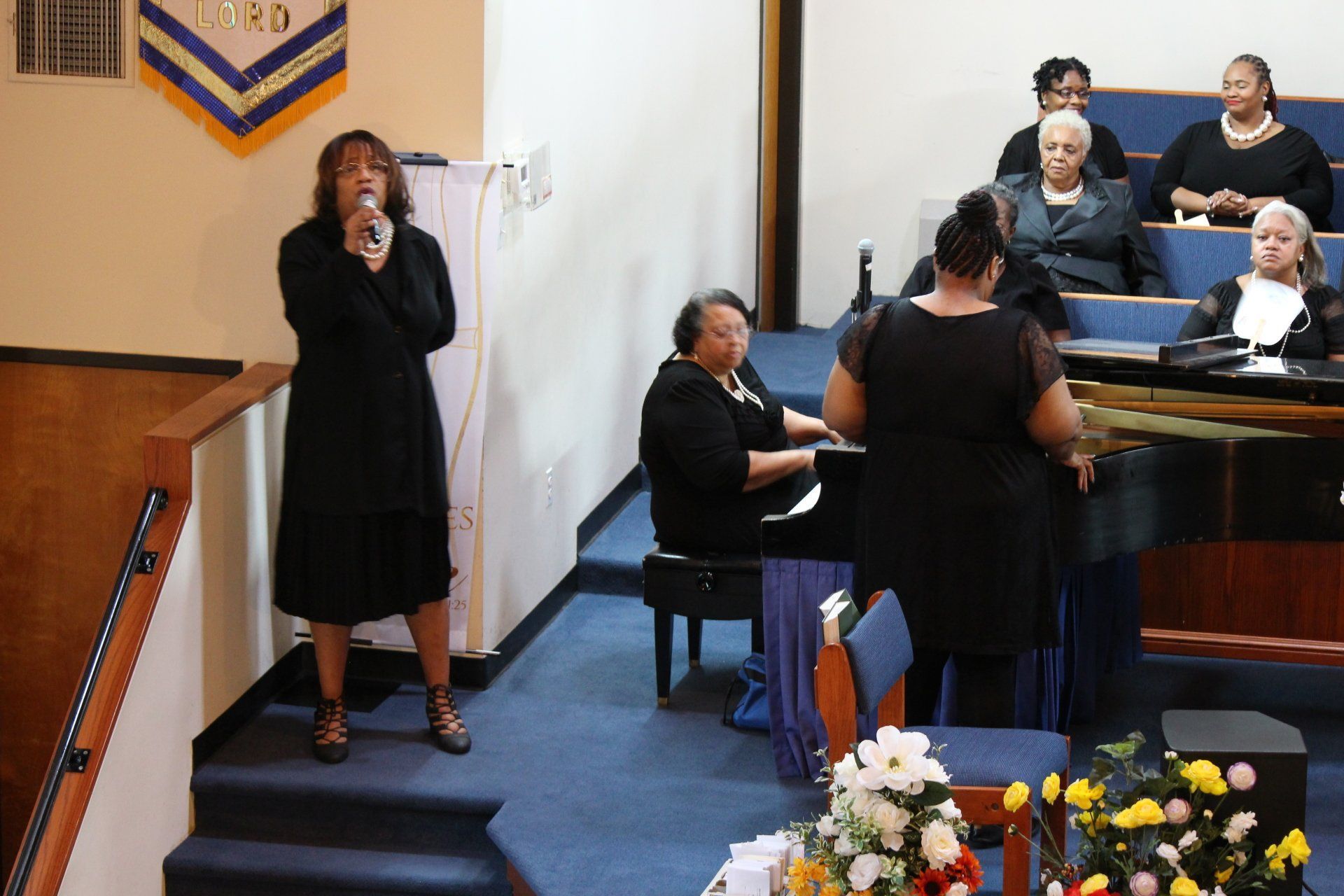 Woman speaking into a microphone at the front of a church or hall during a service
