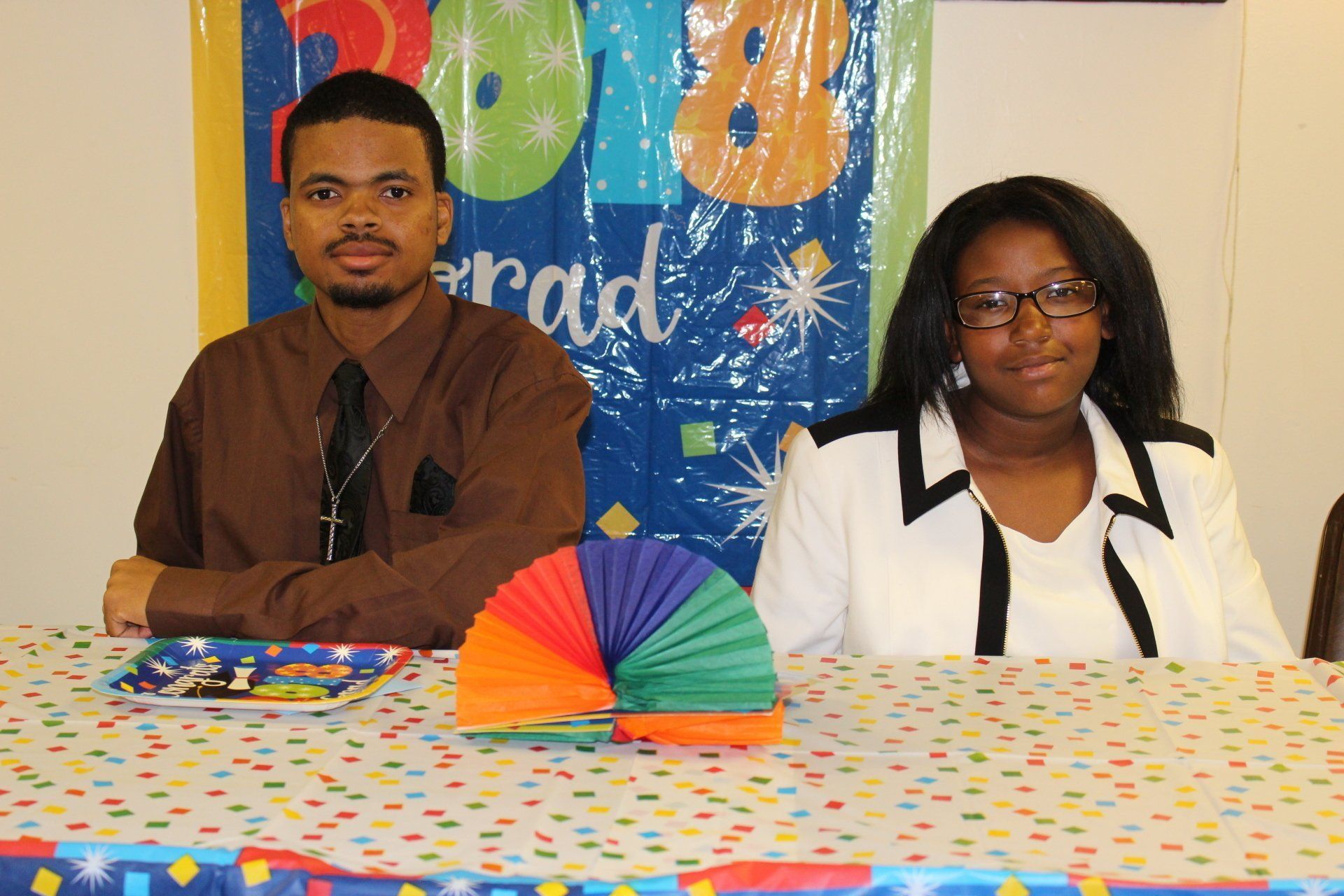 Two people seated behind a polka-dot table with a colorful fan centerpiece at a decorated event table