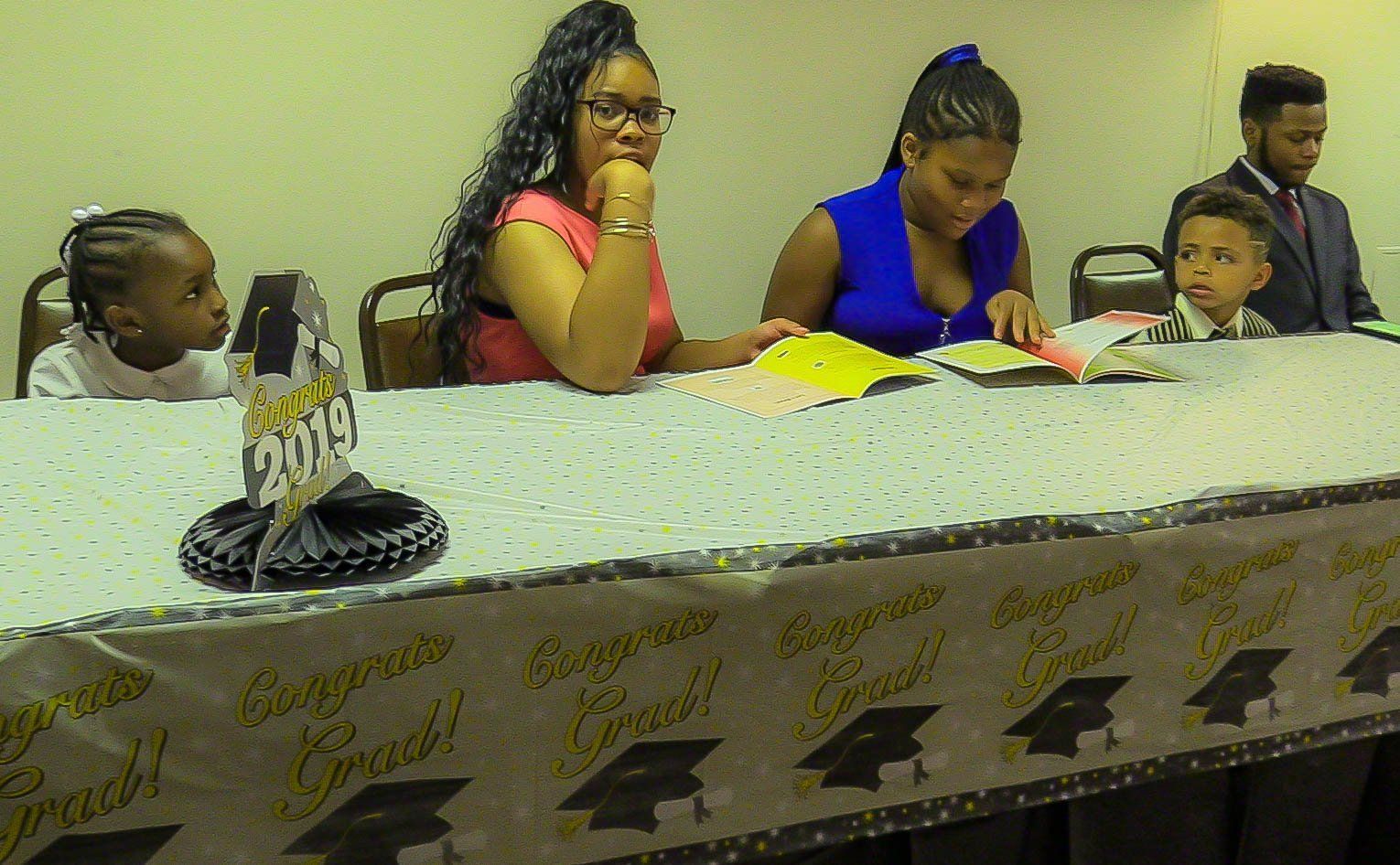 Five people seated behind a decorated table at an event, looking down and writing or reading papers.
