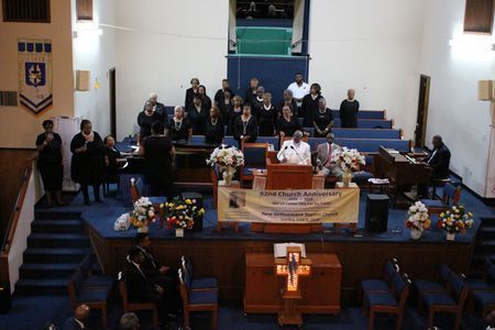 Memorial service in a church with floral arrangements, banners, and people seated around a casket.