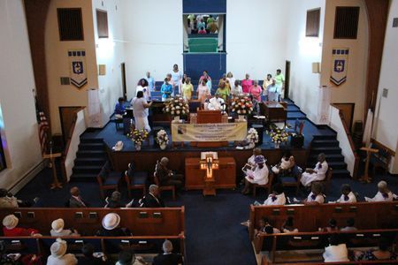 Church service with congregation seated in pews, a choir at the front, and a decorated altar.