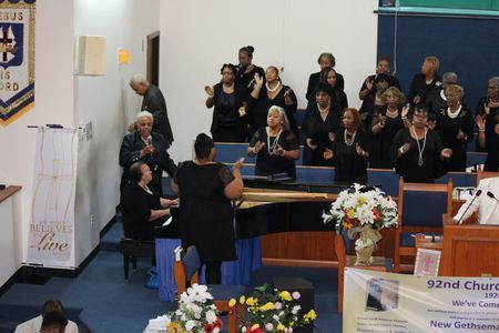 Choir singing in a church sanctuary, with a conductor and flowers at the front altar.