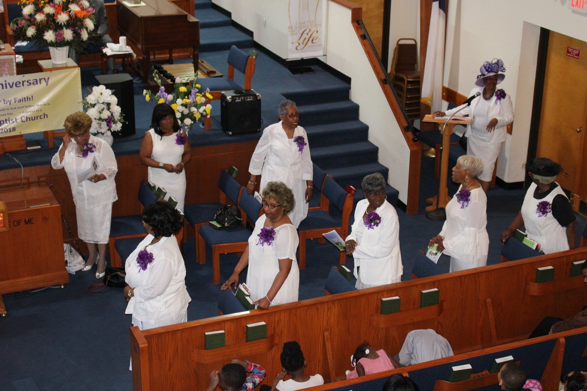 People in white robes standing in a church aisle during a service
