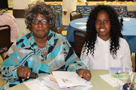 Two people seated at a table, smiling, with papers and cups in a community room