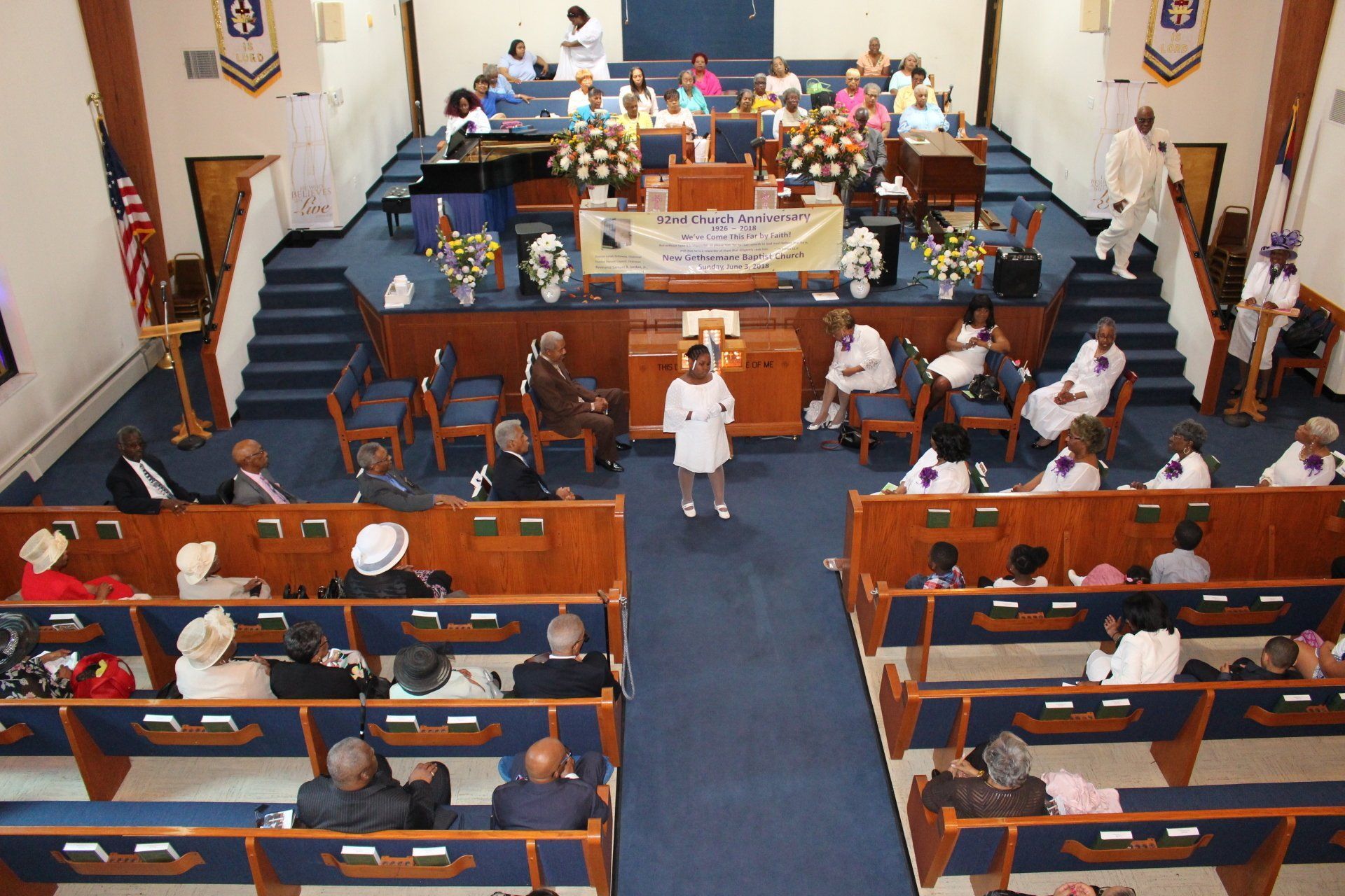 View from balcony of a church service with people seated in pews and a speaker at the front center