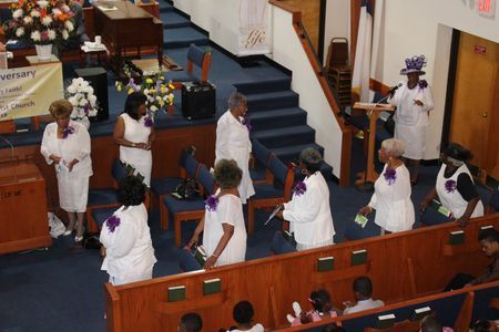 People in white robes walking in a church aisle during a ceremony