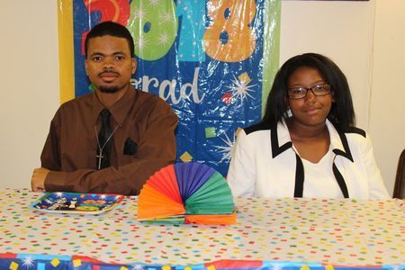 Two people seated behind a polka-dot tablecloth at a decorated table, with a rainbow fan centerpiece.
