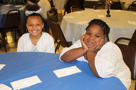 Two children smiling at a blue-covered table in a banquet hall