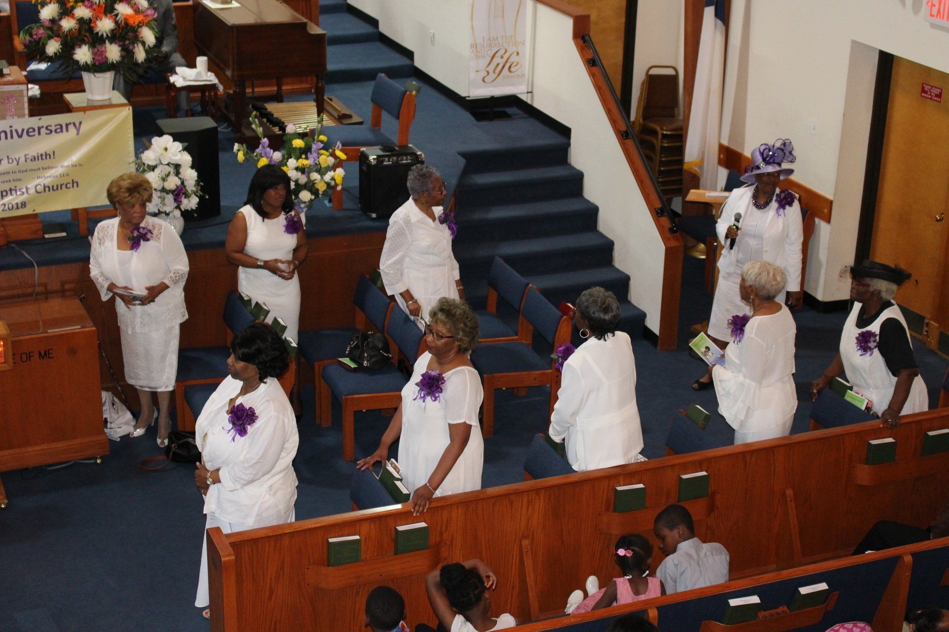 People in white robes stand in church pews during a ceremony, viewed from above.