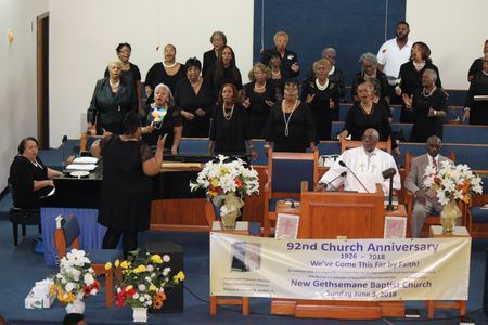 Church choir singing during an anniversary service at the altar with floral arrangements and a banner.