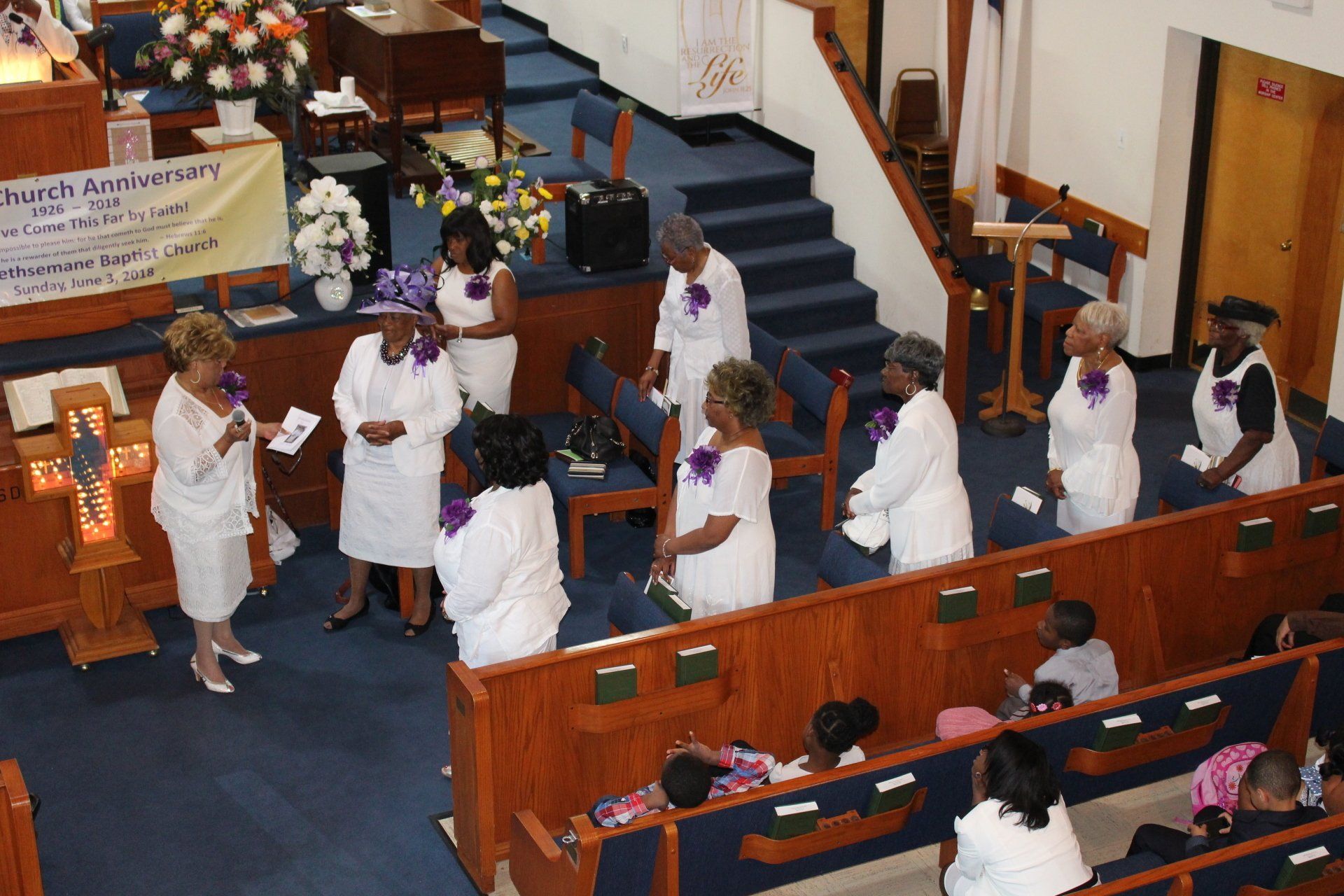 People in white robes gather in a church aisle during a ceremony, with pews and a pulpit visible.