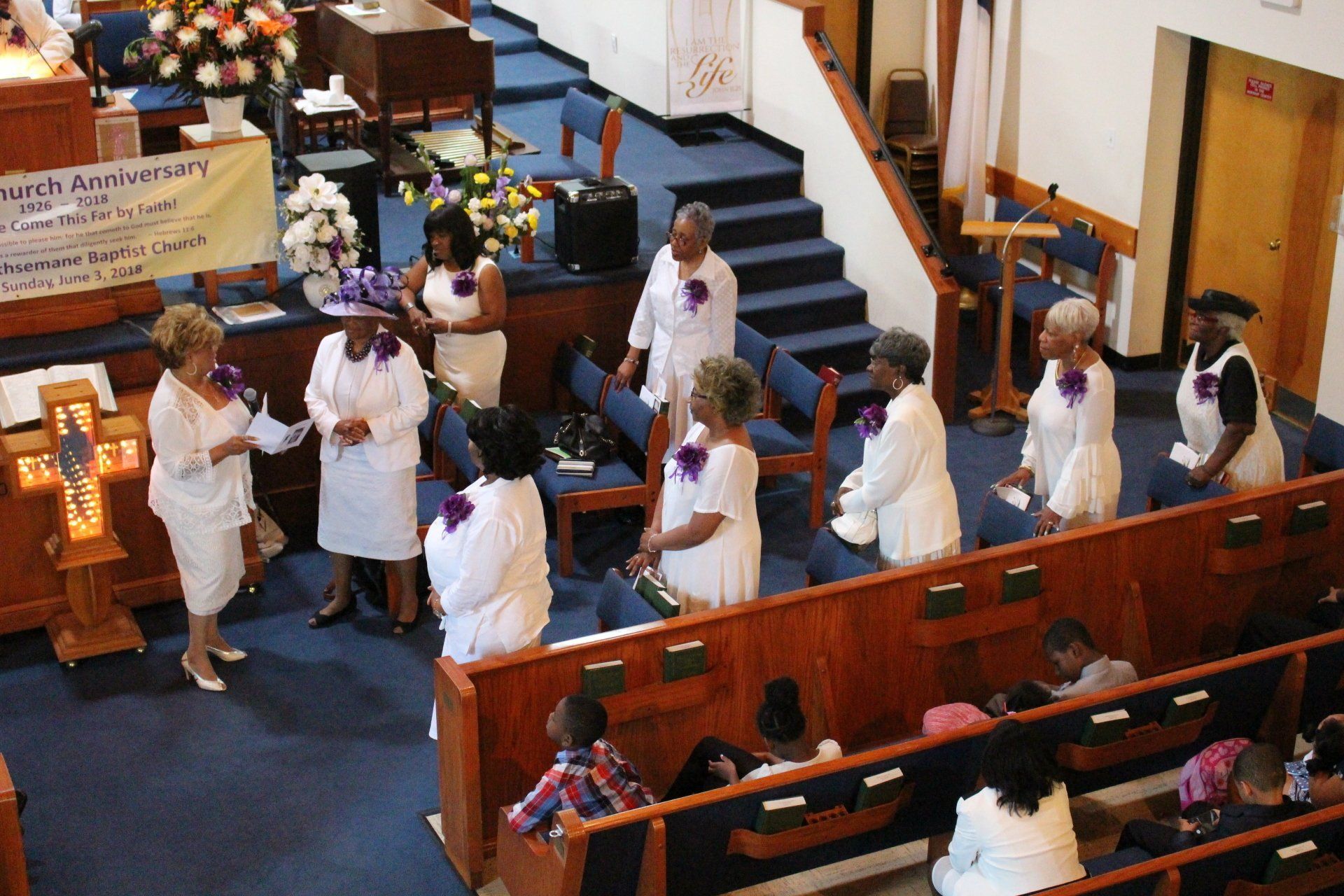 Choir members in white robes perform in a church sanctuary before seated attendees