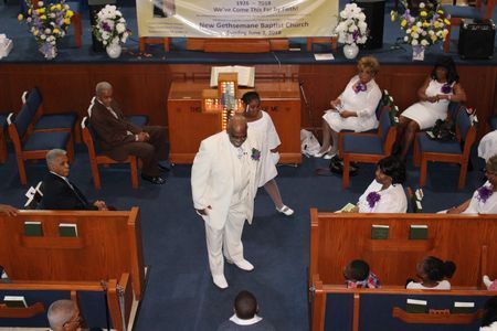 People seated in a church sanctuary with a man in white standing in the aisle.