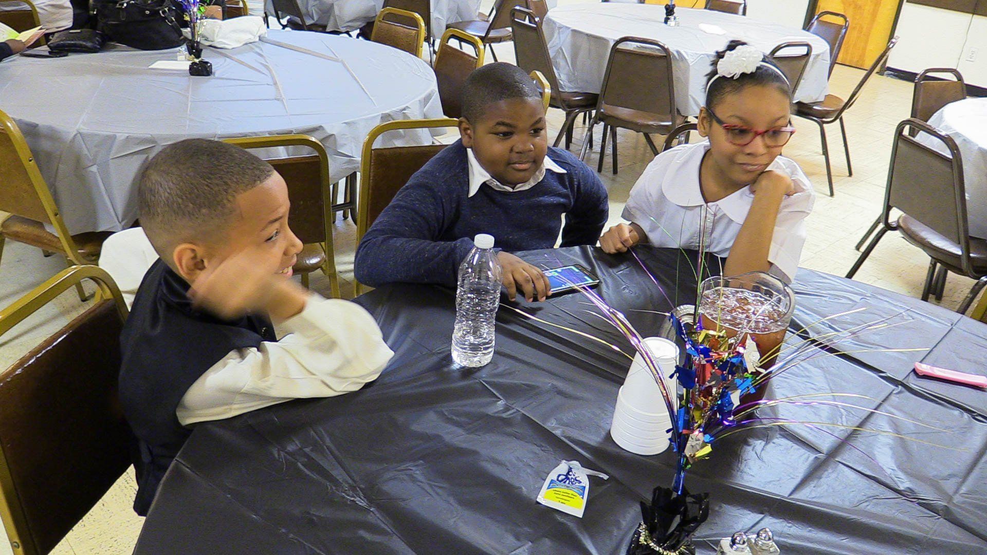 Children seated at a decorated table with snacks and bottles at a party or banquet.
