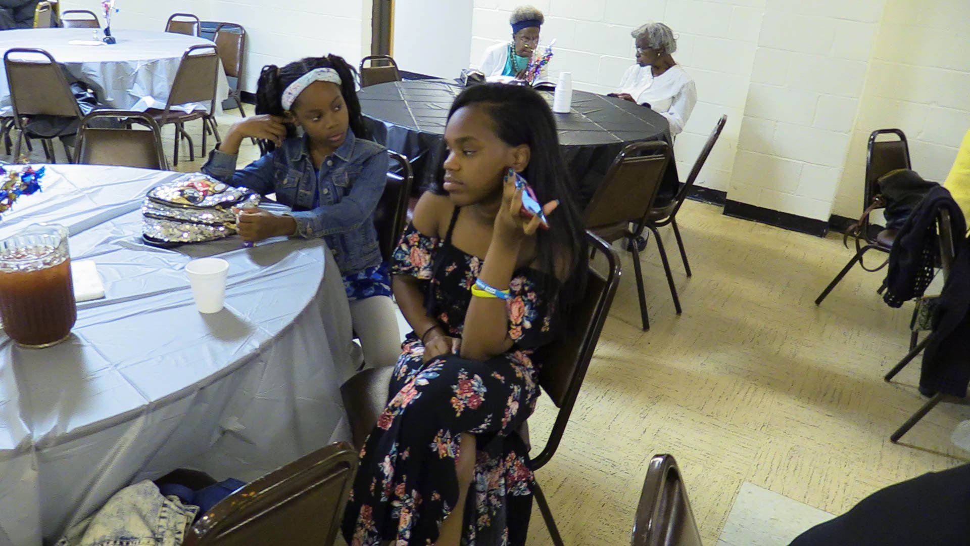 Two children seated at a table in a dining hall, with drinks and trays of food nearby.