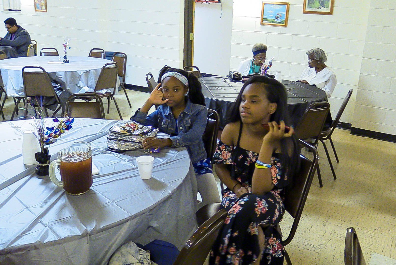 Children seated at a banquet table with drinks and plates in a decorated hall.