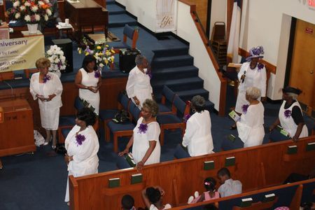 Choir members in white robes standing in a church pew during a service