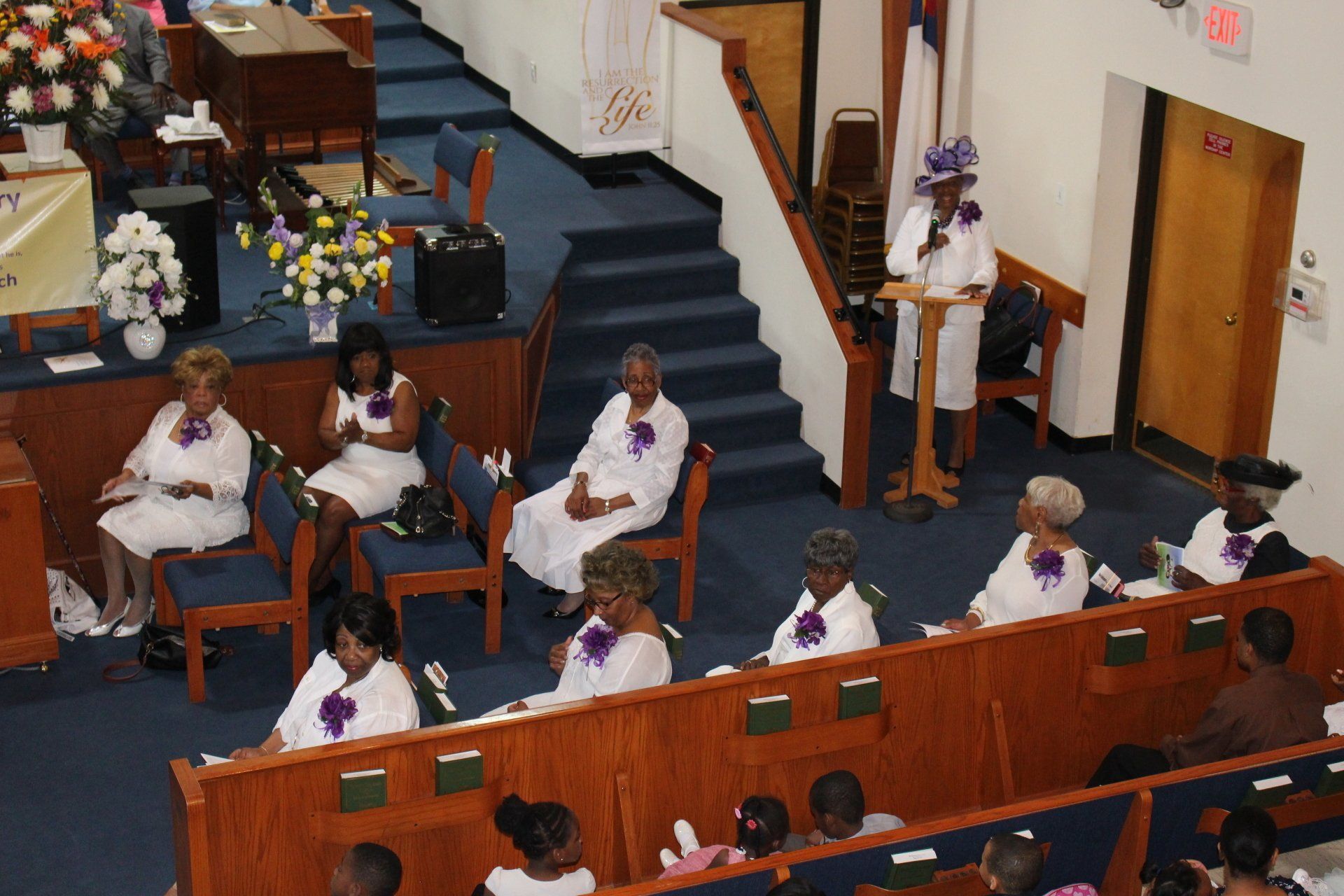 People seated in a church sanctuary near the altar, wearing white robes during a service