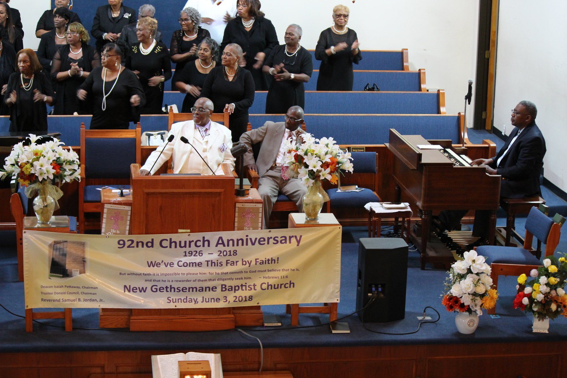 Church anniversary service with speaker at podium, choir seated behind, and banner on the stage