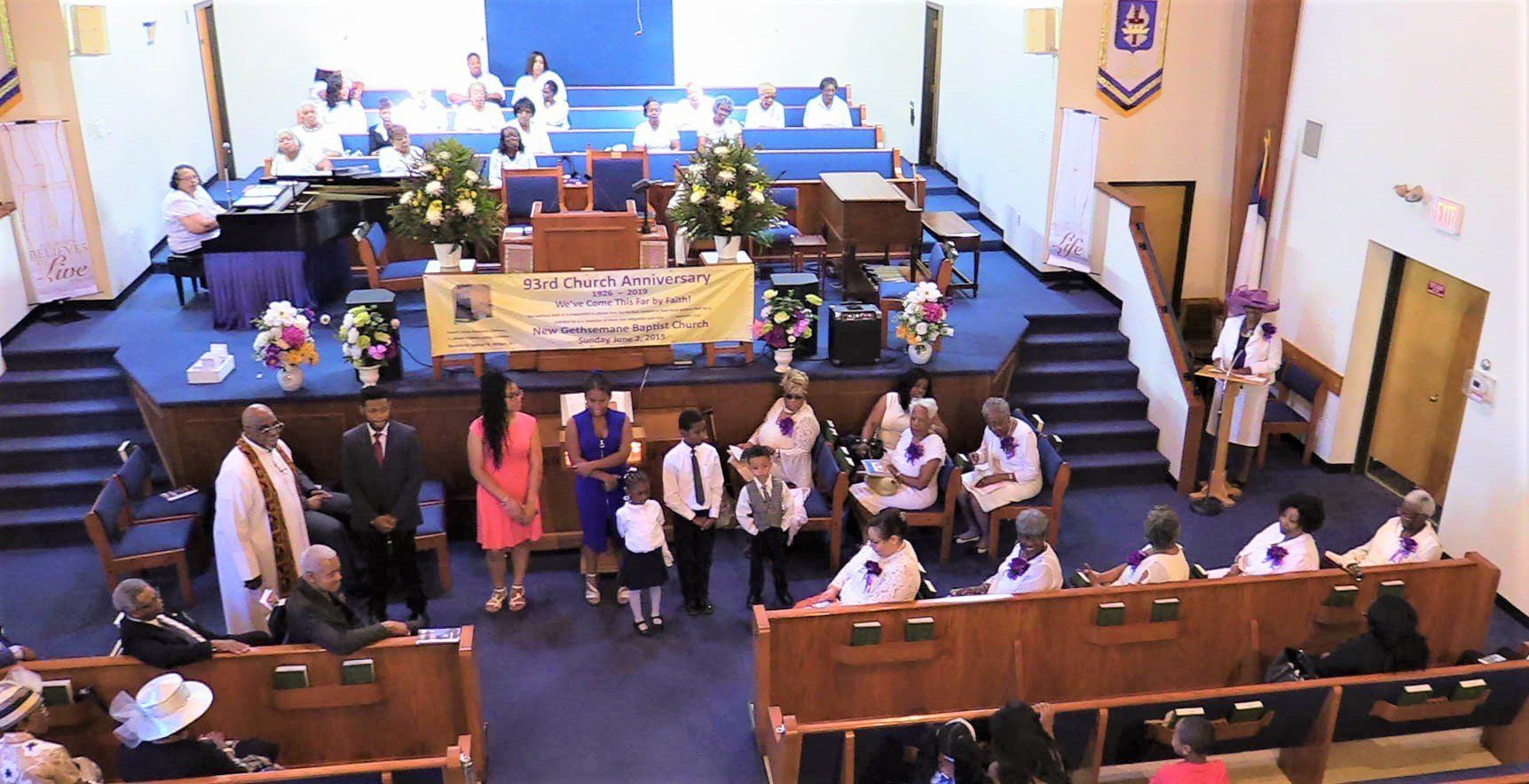 Church sanctuary with people seated and standing near the front stage during a service