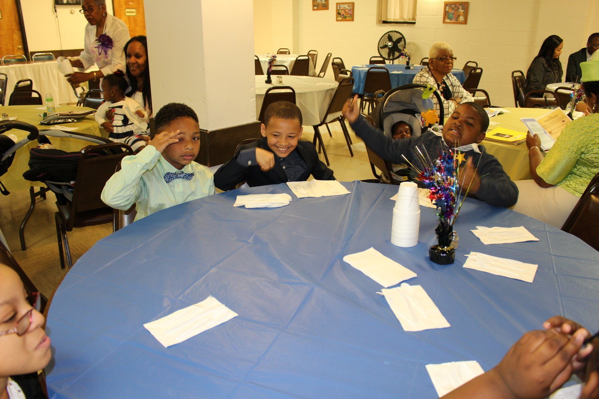 Children seated around a blue table at a classroom activity with papers and cups