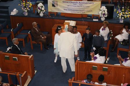 People walking up the aisle in a church sanctuary during a service, with seated attendees and floral decorations.