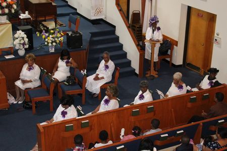 Choir members in white robes seated in a church sanctuary near the pulpit and pews