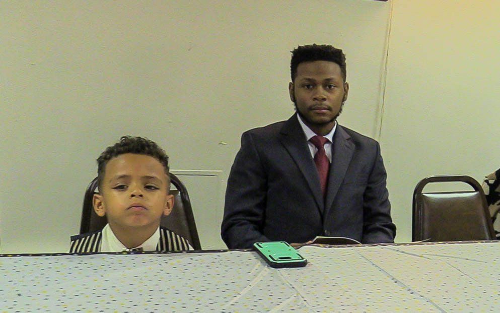 Two people seated at a table in a meeting room, with a phone on the table in front of them.