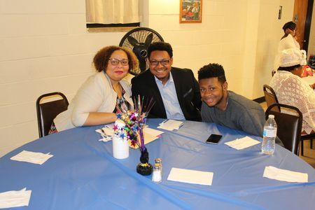 Three people smiling at a banquet table with blue tablecloth and floral centerpiece