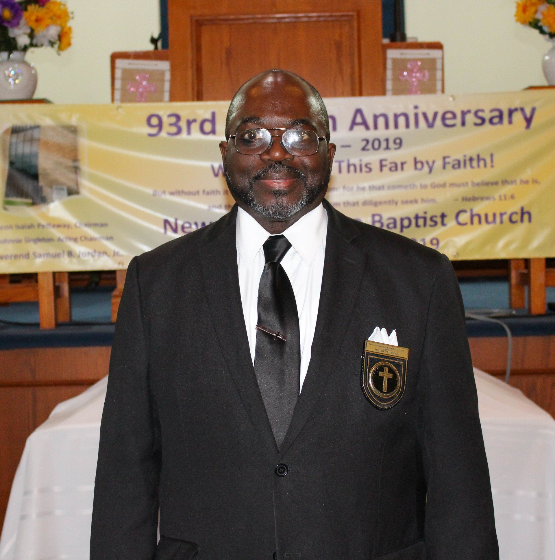 Man in black suit and tie standing in a church before a 93rd anniversary banner