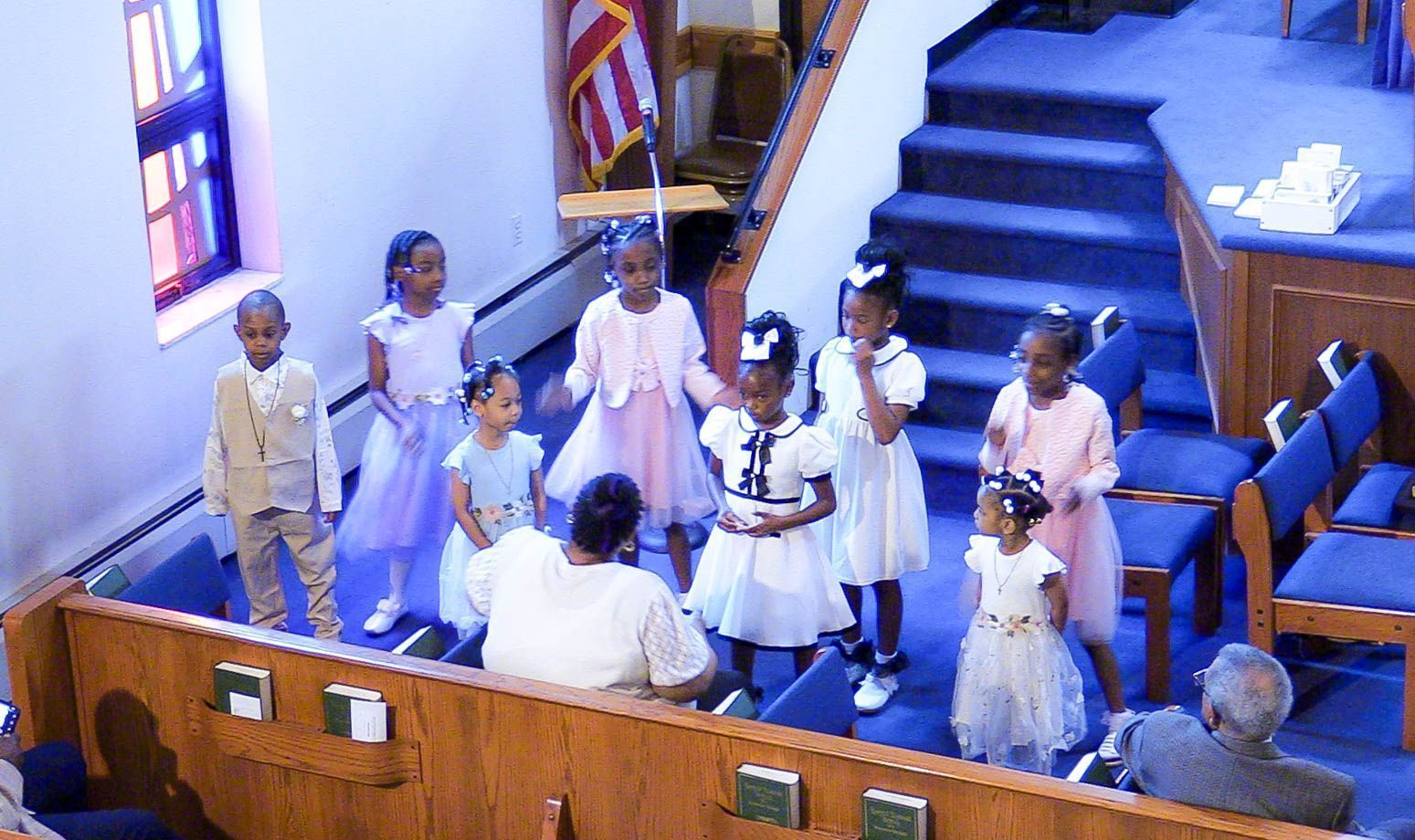 Children standing and singing in a church choir near the front pews and steps