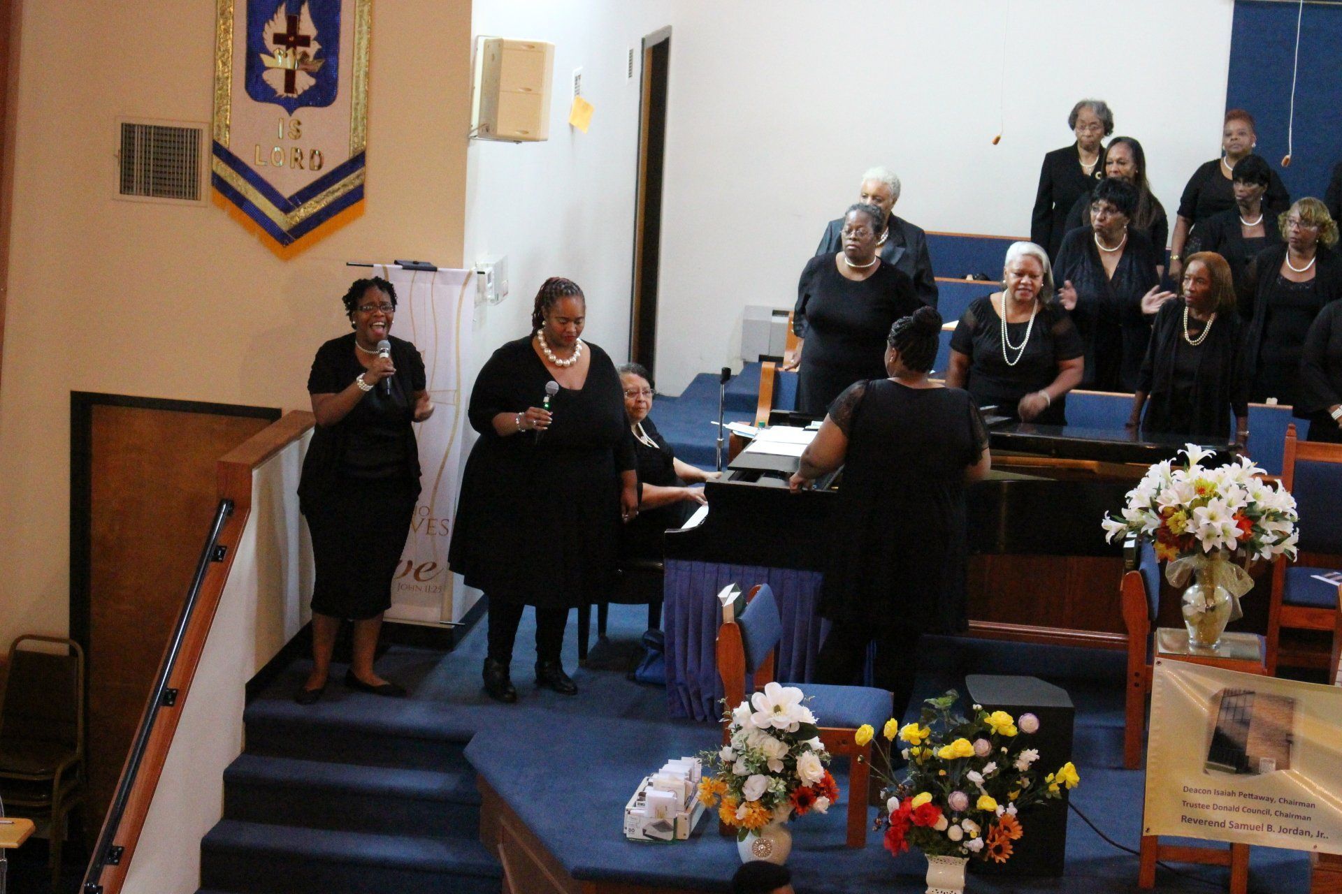 Choir singing in a church sanctuary, with flowers and people seated on risers.