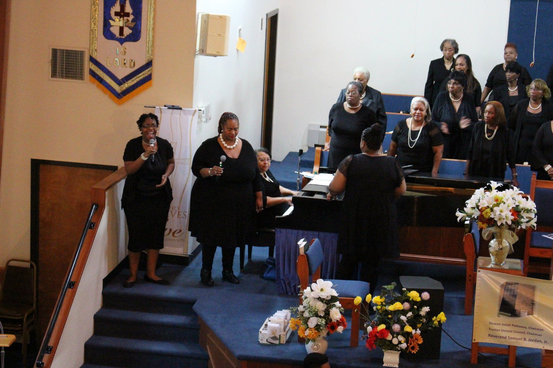 Choir singing on a church stage with floral arrangements and a pulpit during a service