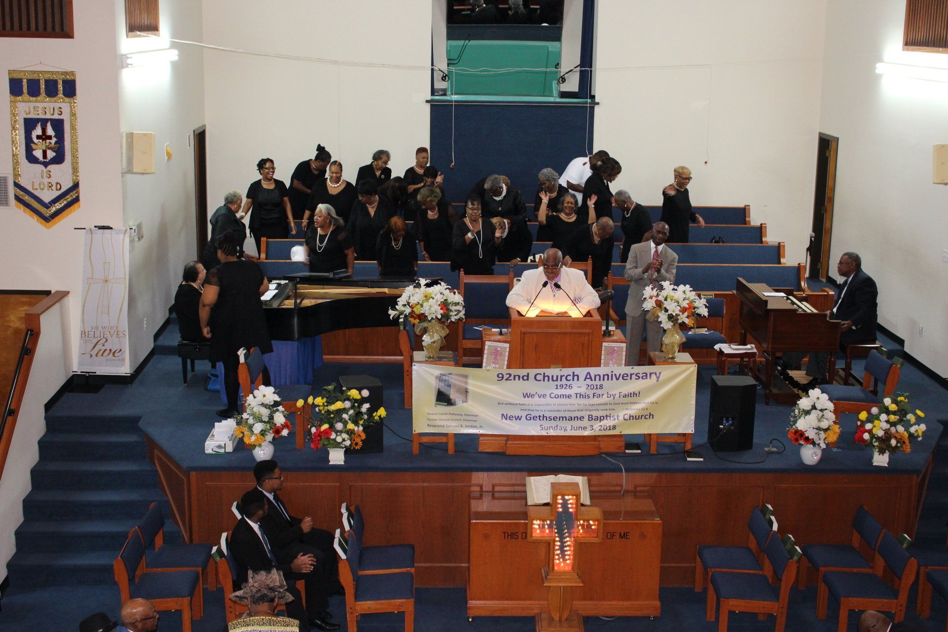 Church service with choir and musicians on a blue stage, banners and flower arrangements at the front