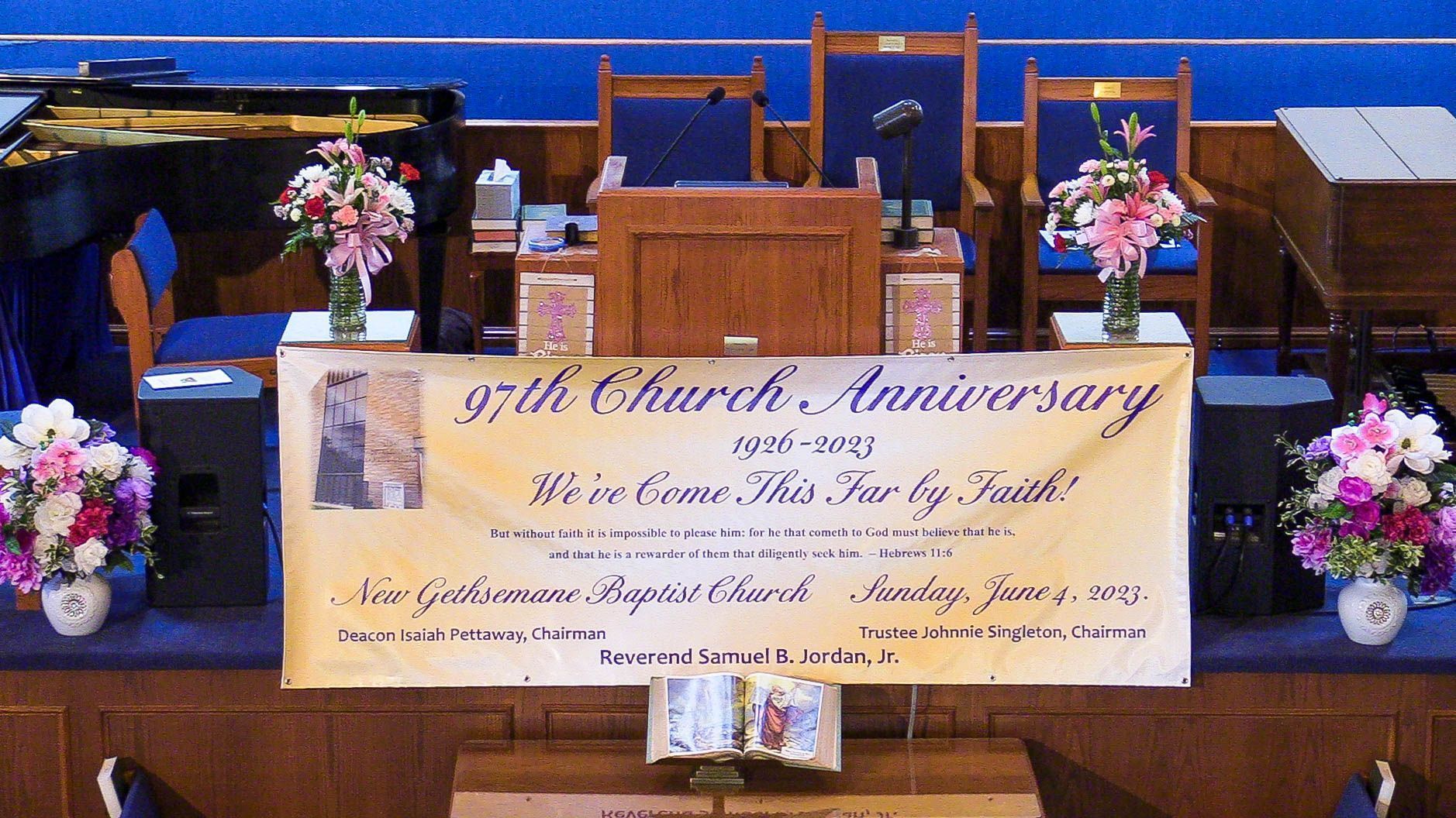 Church anniversary banner on a stage with flowers and wooden chairs behind it